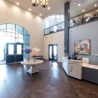 A spacious and modern lobby with a high ceiling, featuring a reception desk, decorative flowers, and a chandelier.