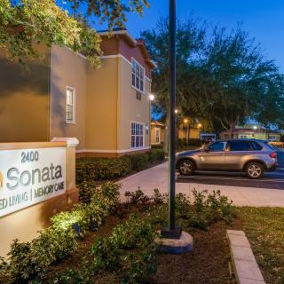 An evening view of an apartment complex with a well-lit entrance and parking area.