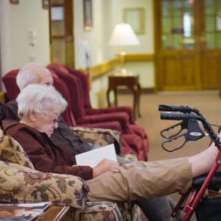 Two seniors relaxing in a cozy common area, one enjoying a book.