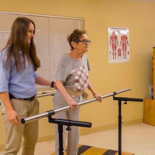 A caregiver assists an elderly woman during a balance training session using support bars.