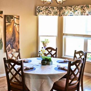 A cozy dining room with a round table set for four, adorned with a floral centerpiece and natural light streaming through the windows.