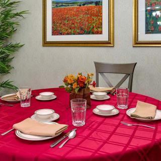 A dining table is elegantly set with a red tablecloth, complete with plates, glasses, napkins, and a central floral arrangement.