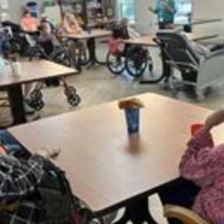 A group of elderly individuals seated around tables in a care facility.