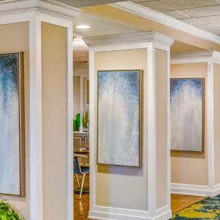 A well-lit hallway featuring abstract paintings and decorative columns.
