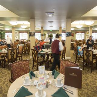 A bustling restaurant dining room with neatly set tables and waitstaff attending to guests.