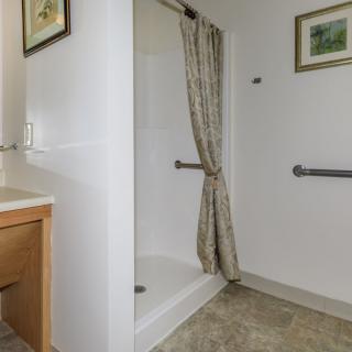 A bathroom with a shower area, curtain, and safety grab bars.