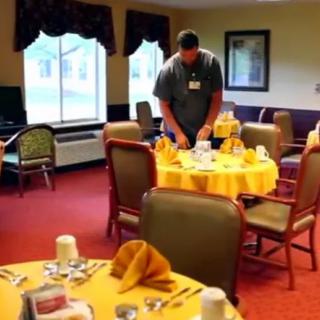A staff member preparing tables in a warmly decorated dining room.