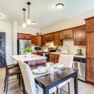 A modern kitchen with wooden cabinets, a central island, and stainless steel appliances, featuring a cozy dining area.