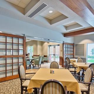 A spacious dining area with neatly arranged tables and chairs, featuring large windows and soft lighting.