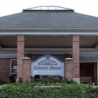 The entrance of a building with the sign 'Colonial Manor' displayed prominently in front.