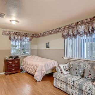 A cozy bedroom with a single bed, sofa, and wooden flooring, featuring two windows with decorative drapes.