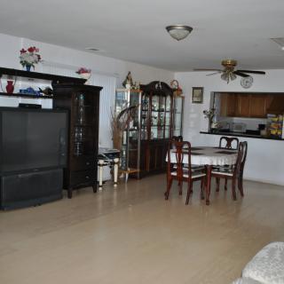 A spacious living and dining area with a large television, wooden furniture, and an open kitchen layout.