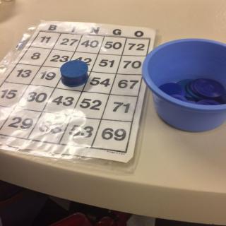 A bingo card with number tokens and a container on a table.