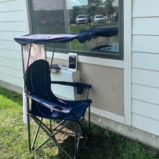 A portable chair with a canopy set up beside a window, perfect for enjoying some shade outdoors.