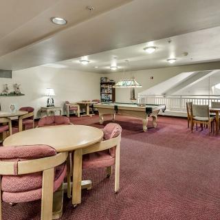 A spacious lounge area with tables and chairs, featuring a carpeted floor and bright lighting.