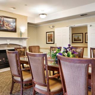 A cozy dining room with a table surrounded by chairs, adorned with flowers and decorative paintings on the walls.