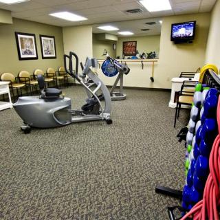 A small gym room equipped with exercise machines and dumbbells, featuring a television on the wall.