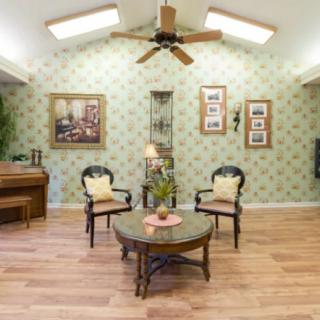 A cozy living room with traditional decor, featuring a ceiling fan, elegant wallpaper, and comfortable seating.