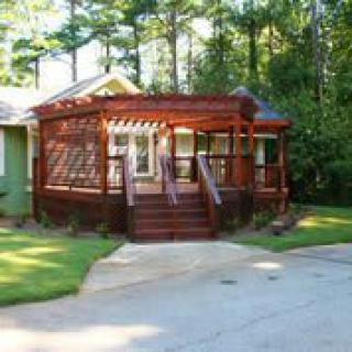 A quaint house with a wooden porch surrounded by trees and a driveway.