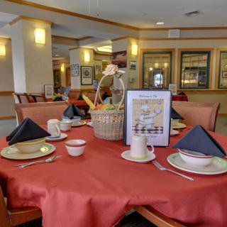 A restaurant dining setup with a red tablecloth, neatly arranged plates and cups, and a decorative basket centerpiece.