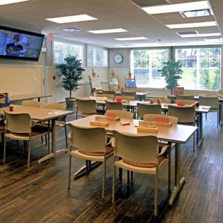 A well-lit classroom with multiple desks and chairs, featuring educational tools like a whiteboard and television.