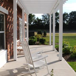 A peaceful porch with a rocking chair under a pergola, overlooking a garden.