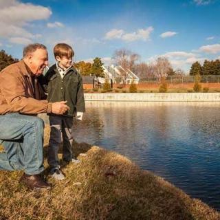 An adult and a child enjoy a moment together by the lake on a sunny day.