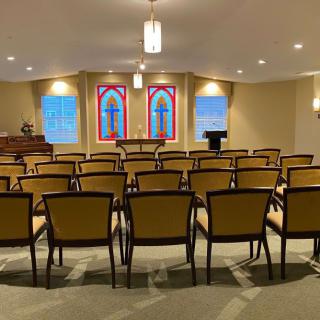 A small chapel interior with rows of chairs facing a stained glass altar.