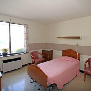 A simple hospital room with a single bed, chairs, and a window.