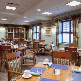 An empty dining area with wooden tables and chairs neatly arranged, set with plates and cutlery.