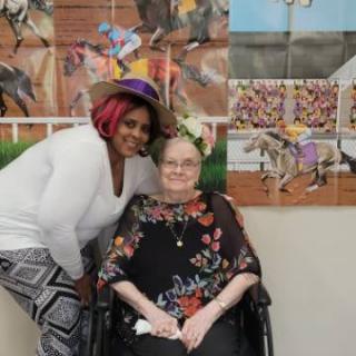 Two people smiling together in front of art, one seated in a wheelchair.
