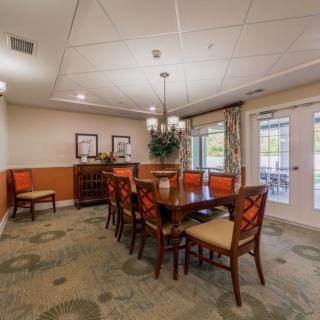 A well-furnished dining room featuring a large wooden table surrounded by chairs, decorative elements, and ample natural lighting from nearby windows.