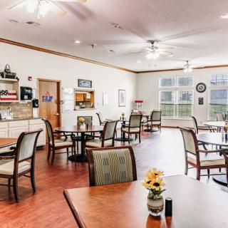A bright and inviting dining area with multiple tables and chairs, featuring large windows and ceiling fans.