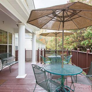 A wooden patio deck with metal furniture and large umbrellas offers a comfortable outdoor seating area amidst surrounding trees.