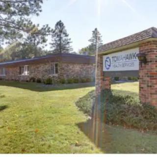 A clinic building with a sign outside surrounded by grass and trees.