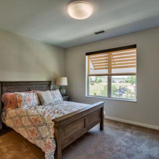A cozy bedroom featuring a bed with colorful bedding, a bedside lamp, and a window with blinds.