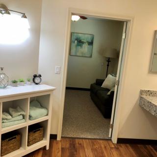 A view from a bathroom with shelves and a mirror, looking into an adjacent living room.
