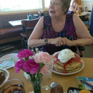 A woman enjoying a meal with pancakes topped with cream at a restaurant table adorned with flowers.