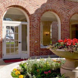 A charming brick building with arched windows and a welcoming entrance, surrounded by a colorful garden.