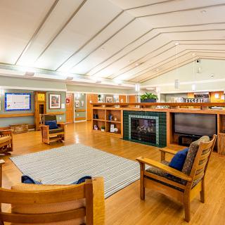 A modern library interior with wooden furniture and bookshelves, featuring a fireplace.
