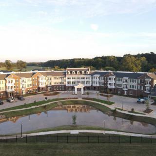 A picturesque view of a residential and commercial building complex with a central pond, surrounded by greenery at sunset.