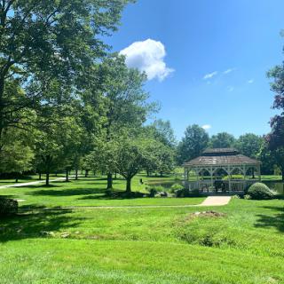 A serene park scene featuring lush greenery and a charming gazebo under a clear blue sky.