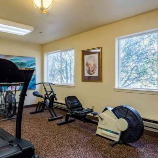 A small gym space featuring a treadmill and stationary bikes, with natural light coming through the windows.