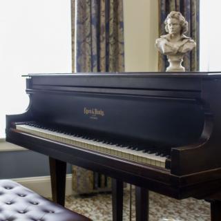 A classic grand piano in a well-appointed music room, adorned with a bust on top.