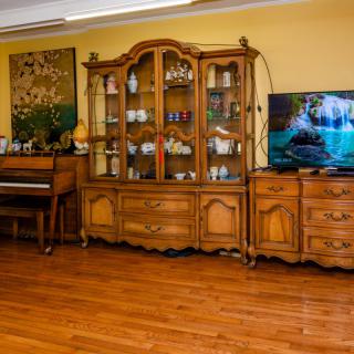 A cozy living room featuring antique wooden furniture, a piano, and a television.