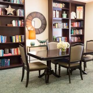 A cozy library with a dining table surrounded by bookshelves filled with books and decorative items.