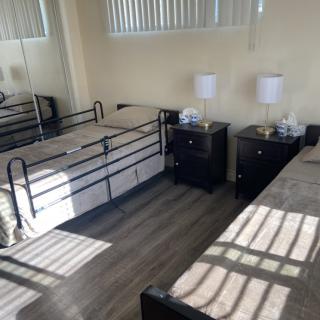 A tidy bedroom featuring two beds, nightstands with lamps, a mirrored wardrobe, and window blinds casting shadows on the floor.