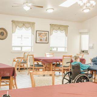A tranquil dining area with tables, chairs, and an elderly person in a wheelchair.