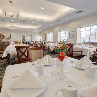 A well-lit dining room with tables set with white tablecloths and neatly arranged napkins.