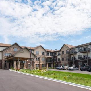 A suburban apartment building with a parking lot under a partly cloudy sky.